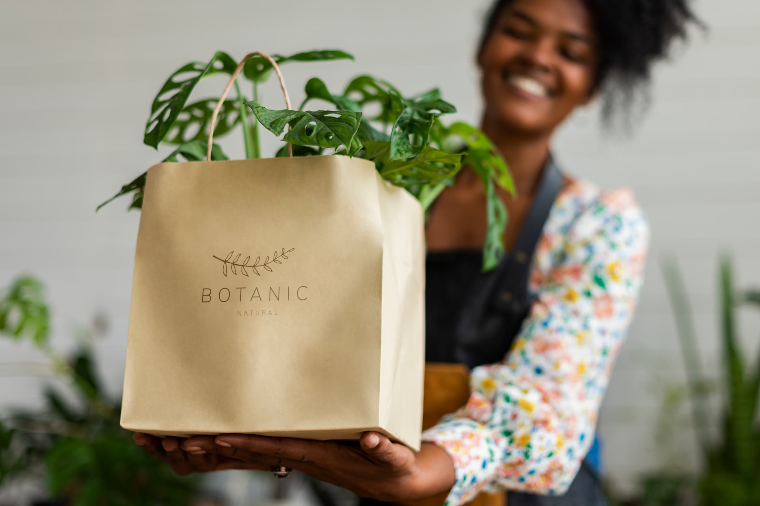A lady holding out a custom printed brown bag, with a plant in it